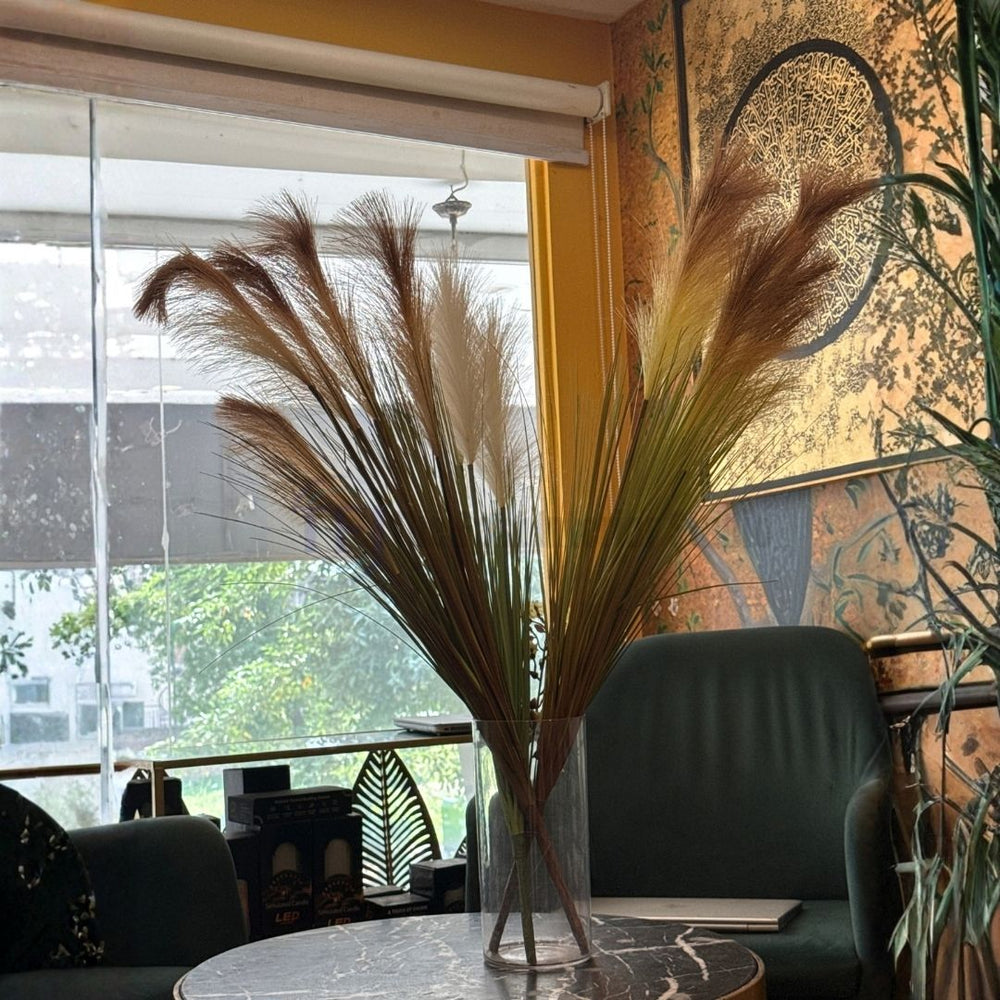 The best 2 foot 2 inch tall artificial pampas grass featuring brown and cream plumes, styled in a glass vase on a marble table in Lahore