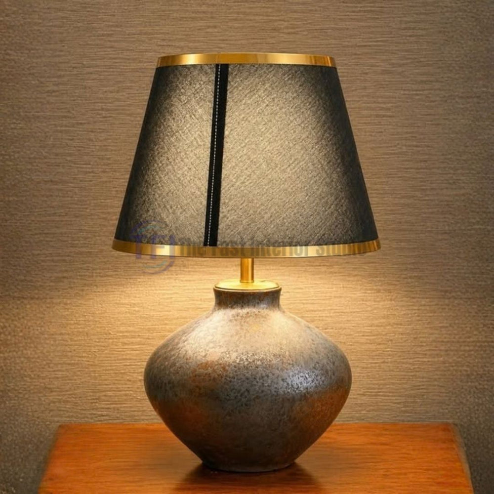 The best luxury metallic ceramic table lamp featuring a textured base and a black shade with gold rims, styled on a wooden surface for versatile home decor