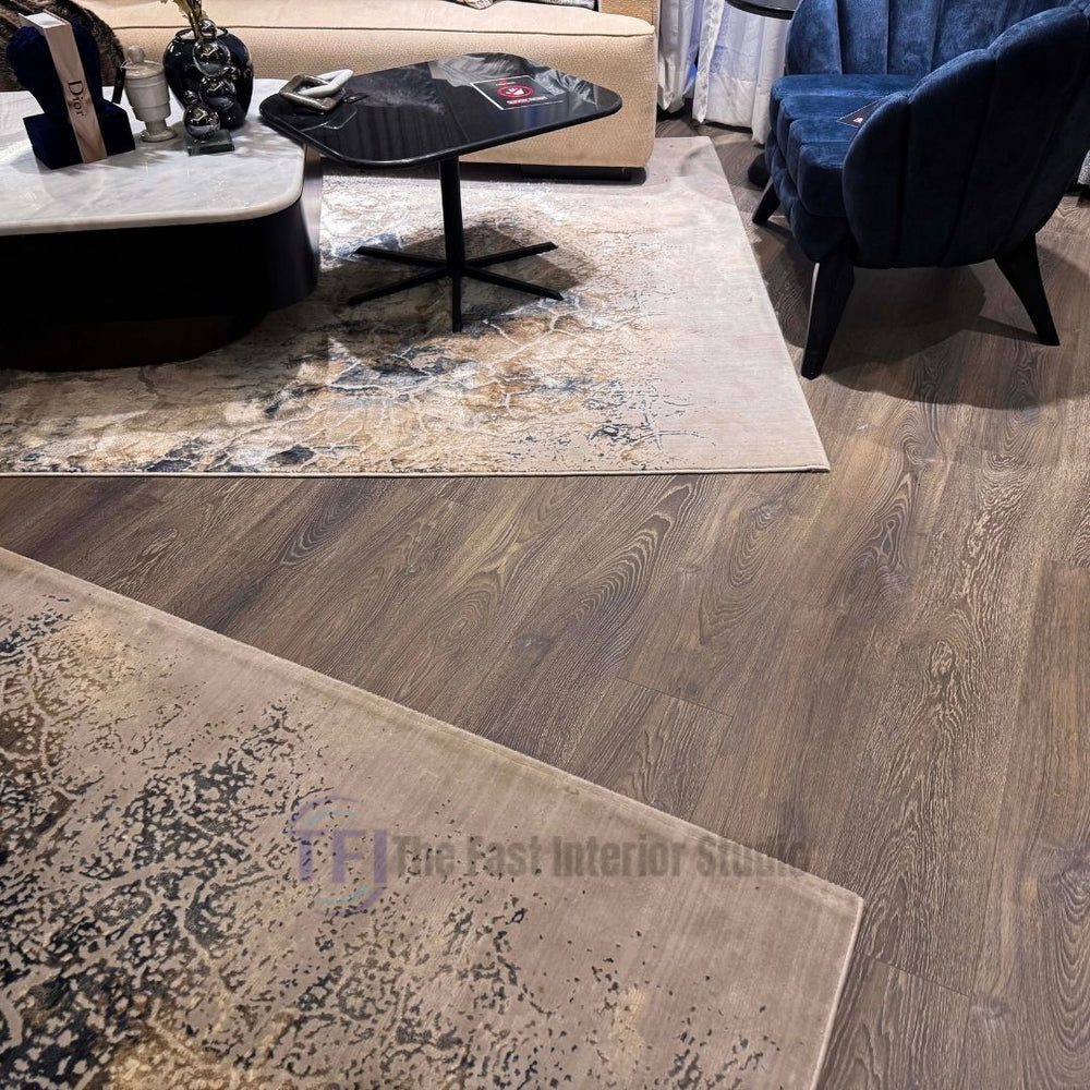 Warm grey-brown wood laminate planks seamlessly installed next to distressed abstract area rugs and a modern navy blue velvet chair